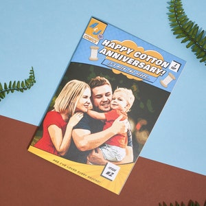 May include: A comic book style card with a photo of a family of three. The card is blue and yellow with the text "Happy Cotton Anniversary! It's been two years... and I've loved every second!" The card is titled "Happy Cotton Anniversary!" and has the text "Issue #2" in the bottom right corner.