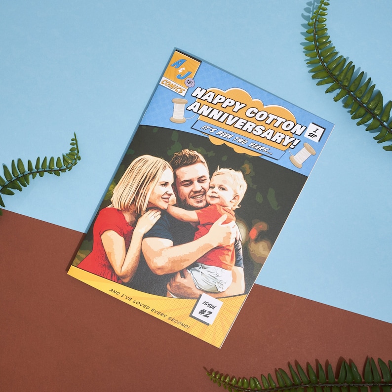 May include: A comic book style card with a photo of a family of three. The card is blue and yellow with the text "Happy Cotton Anniversary! It's been two years... and I've loved every second!" The card is titled "Happy Cotton Anniversary!" and has the text "Issue #2" in the bottom right corner.