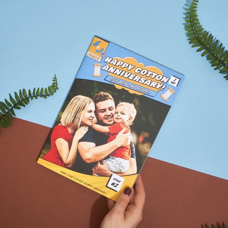 May include: A comic book cover with a photo of a family of three. The cover is blue and yellow with the text "Happy Cotton Anniversary! It's been two years..." and "Issue #2".