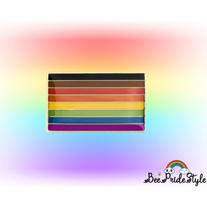 May include: A rectangular enamel pin featuring the Progress Pride flag design. The pin has a gold border and includes the traditional rainbow colors, plus black, brown, light blue, pink, and white. The pin is set against a rainbow gradient background.