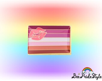May include: A rectangular pin featuring the lesbian pride flag design with a gold border. The flag has horizontal stripes in shades of pink, red, and orange, with a pair of lips in the upper left corner. The background is a rainbow gradient.