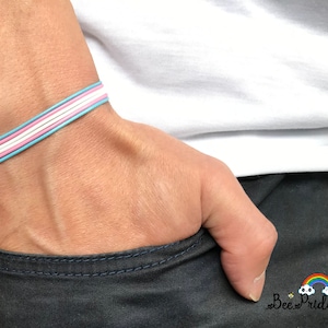 May include: A woven bracelet in blue, pink and white. The bracelet is being worn on someone's wrist.