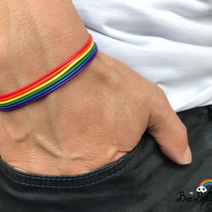 May include: A rainbow colored bracelet made of thin cords. The bracelet is worn on a person's wrist.