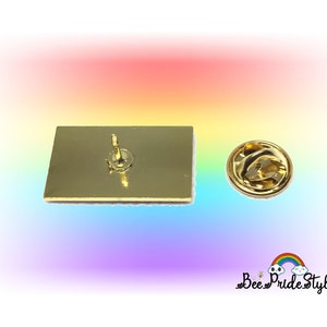 May include: A gold-colored rectangular pin with a pin back and a separate clasp. The pin has a rainbow-colored border. The text "Bee Pride Style" is visible in the lower right corner.