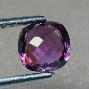 Pu&ograve; includere: Una pietra preziosa di ametista rotonda e sfaccettata con una tonalit&agrave; viola. La pietra preziosa &egrave; tenuta da una pinzetta.