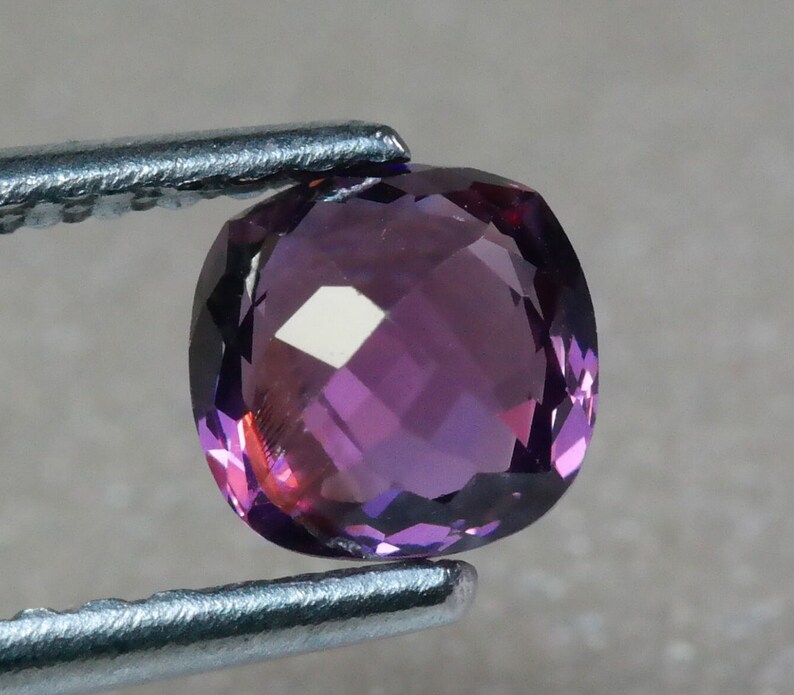 Pu&ograve; includere: Una pietra preziosa di ametista rotonda e sfaccettata con una tonalit&agrave; viola. La pietra preziosa &egrave; tenuta da una pinzetta.