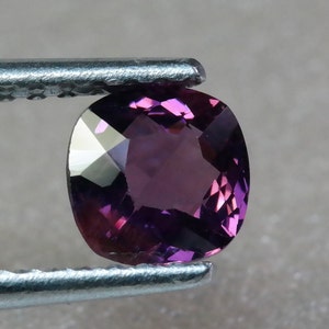 Pu&ograve; includere: Una gemma viola vibrante con forma ovale sfaccettata, tenuta in una pinza.