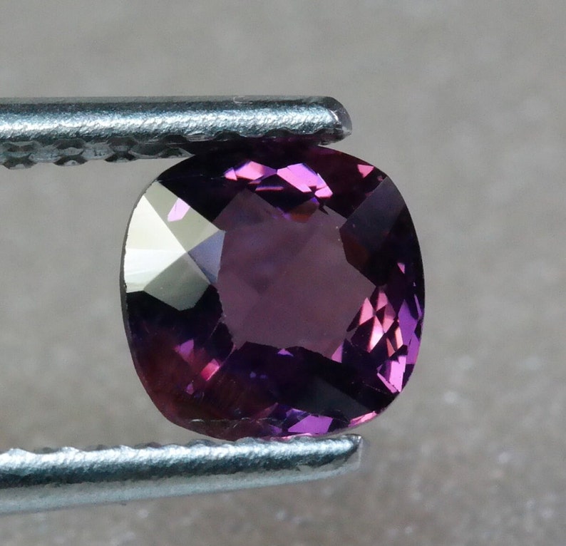 Pu&ograve; includere: Una gemma viola vibrante con forma ovale sfaccettata, tenuta in una pinza.