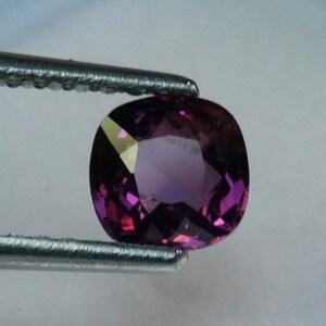 Pu&ograve; includere: Una pietra preziosa ovale di colore viola con sfaccettature, tenuta da una pinzetta.