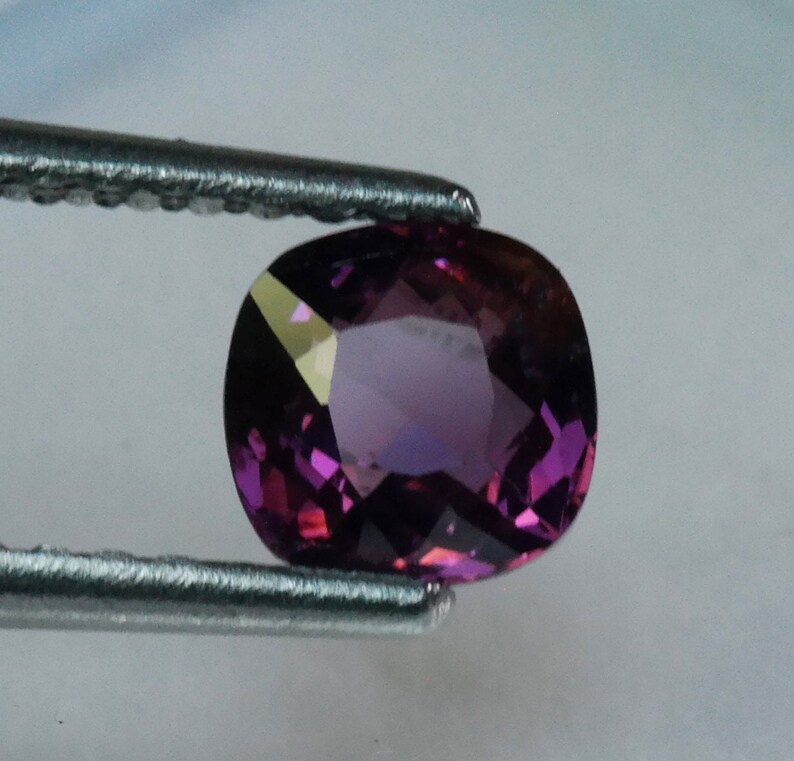 Pu&ograve; includere: Una pietra preziosa ovale di colore viola con sfaccettature, tenuta da una pinzetta.