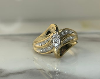 May include: A gold ring with a marquise-shaped diamond in the center and smaller diamonds set in a wave pattern around the band.