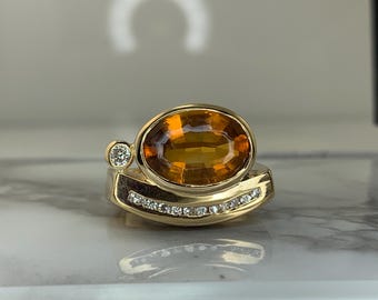 May include: A gold ring with a large oval-shaped orange gemstone and smaller round diamonds set in the band.