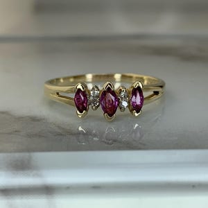 Peut inclure: Une bague en or ornée de trois pierres précieuses roses en forme de marquise et de deux petites pierres rondes et transparentes. La bague a un design à tige fendue. Les pierres sont disposées en rangée.