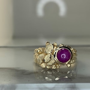 May include: A gold ring with a textured band and a large, round, cabochon-cut ruby gemstone.