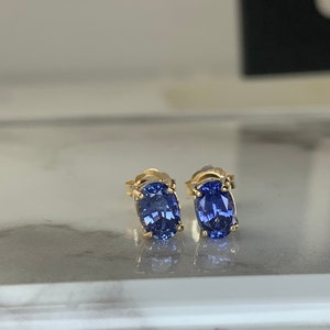 May include: A pair of gold stud earrings with oval-shaped blue gemstones.