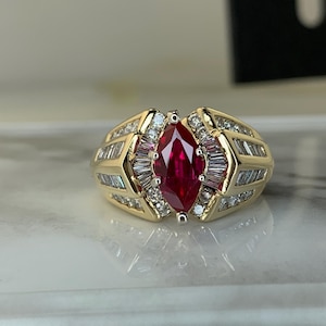 May include: A gold ring featuring a large, marquise-cut ruby center stone. The ring is accented with smaller, baguette-cut diamonds and round diamonds, set in a gold band. The ring has a classic, elegant design.