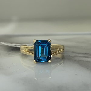 May include: A gold ring with a blue topaz gemstone. The ring has a split shank design.