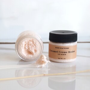 Może przedstawiać: Mały słoiczek r&oacute;żowego peelingu do ust z etykietą "Sudsy Soap Works Caramel Creme Brulee Lip Scrub Net Wt 1 oz".