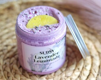 Może przedstawiać: Szklany słoik z mydłem do ciała z lawendy i limonady, z plasterkiem cytryny na wierzchu. Słoik ma białą etykietę z tekstem "Sudsy Soap Works Lavender Lemonade Whipped Soap Scrub".
