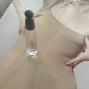 May include: A clear glass bottle with a black cap and a textured surface. The bottle is empty and appears to be a perfume bottle.