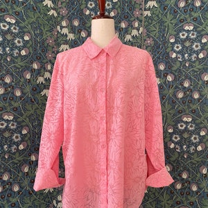 May include: A pink button-down shirt with a floral pattern. The shirt has long sleeves and a collared neckline.