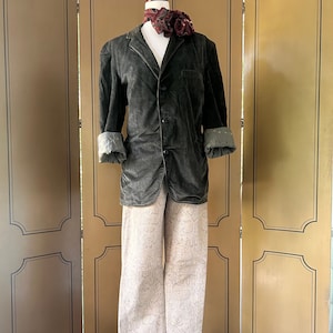 May include: A green corduroy blazer with a button closure and a patterned scarf. The blazer is worn over a pair of beige trousers with a snake print.
