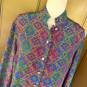 May include: A long-sleeved button-up shirt with a colorful geometric pattern in shades of blue, purple, green, and gold. The shirt has a mandarin collar and pink buttons.