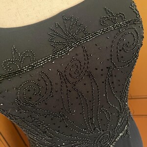 May include: Black evening gown with intricate beadwork. The dress features a scoop neckline and detailed patterns of beads across the bodice. The beading creates a textured, elegant design, perfect for formal events.