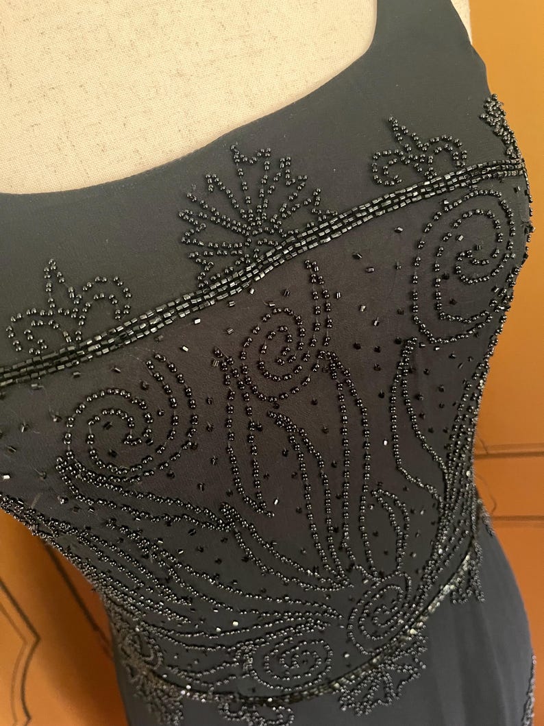 May include: Black evening gown with intricate beadwork. The dress features a scoop neckline and detailed patterns of beads across the bodice. The beading creates a textured, elegant design, perfect for formal events.