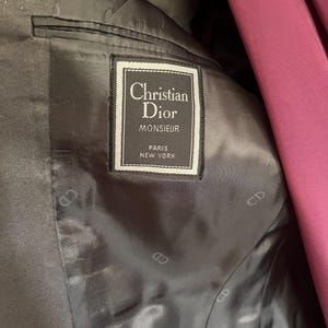 Pu&ograve; includere: Primo piano dell'interno di un blazer Christian Dior Monsieur grigio scuro. L'etichetta recita "Christian Dior MONSIEUR PARIS NEW YORK" in una cornice bianca e nera. La fodera &egrave; grigio scuro con un sottile motivo "CD".