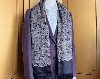 May include: A purple wool suit with a matching skirt and jacket, paired with a white blouse and a patterned scarf. The scarf features a black border with fringe and a floral design in black, gray, and purple.