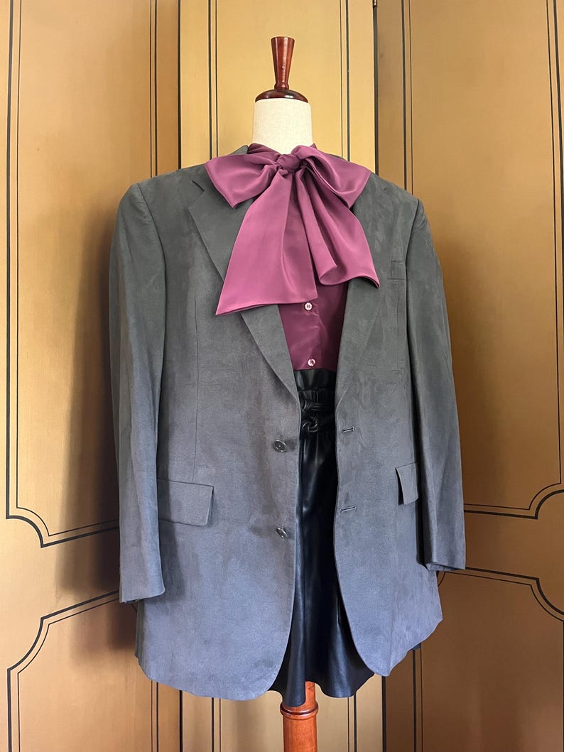 Pu&ograve; includere: Un blazer grigio con un papillon bordeaux e una camicia abbinata. Il blazer ha due bottoni e due tasche. L'outfit &egrave; esposto su un manichino.