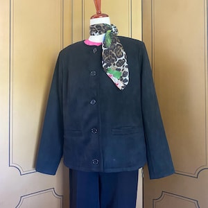 May include: A black suede jacket with a round collar and button closure, paired with matching black pants. A patterned scarf with animal print and floral accents is draped around the neck. The outfit is displayed on a mannequin.