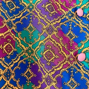 May include: A close-up of a fabric with a colorful geometric pattern. The fabric is a mix of blue, purple, green, and yellow. The pattern is made up of repeating squares and diamonds. There are two pink buttons on the fabric.