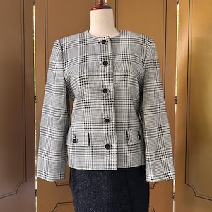 May include: A black and white houndstooth patterned blazer with a round neckline and four black buttons. The blazer has two pockets on the front and is on a mannequin.