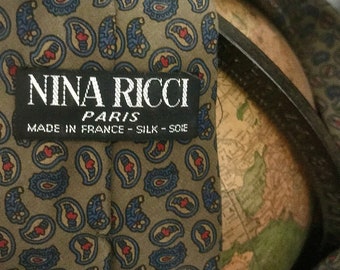 May include: A green silk tie with a paisley pattern and red hearts. The tie has a label that reads "Nina Ricci Paris - Silk - Soie" and "Made in France".