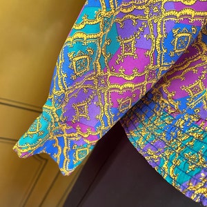 May include: A blue, purple, and gold patterned fabric with a geometric design. The fabric has a ruffled edge.
