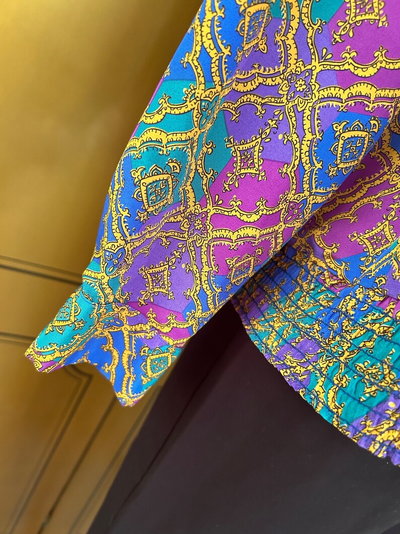 May include: A blue, purple, and gold patterned fabric with a geometric design. The fabric has a ruffled edge.