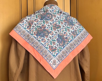 Puede incluir: Chaqueta color canela con una bufanda estampada. La bufanda tiene un fondo blanco con diseños de cachemira azules, verdes y naranjas. La bufanda está bordeada con un borde rosa coral.