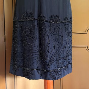 May include: A dark navy blue dress with intricate beaded embellishments. The dress features a detailed pattern of swirling designs and floral motifs along the hemline. The beading adds texture and visual interest to the elegant garment.