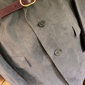 Pu&ograve; includere: Un blazer grigio con due bottoni e una cintura bordeaux con fibbia dorata. Il blazer ha due tasche e una morbida texture simile alla pelle scamosciata. La cintura &egrave; stretta in vita.