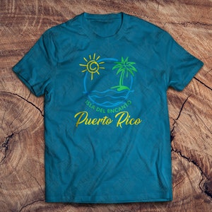 May include: A teal blue t-shirt with a graphic design of a palm tree, sun, and waves. The text "Isla del Encanto Puerto Rico" is printed in yellow and green.