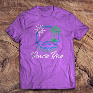 May include: Purple t-shirt with a white graphic of a sun, palm tree, and waves in a circle. The text "Isla del Encanto Puerto Rico" is below the graphic.