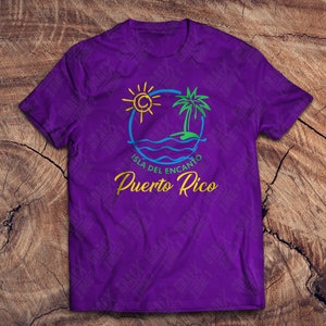May include: Purple t-shirt with a graphic design of a sun, palm tree, and waves. The text "Isla del Encanto Puerto Rico" is written in yellow below the graphic.