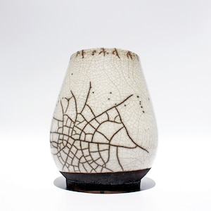 Könnte beinhalten: Eine weiße Keramikvase mit craquelé-Glasur und braunem Rand. Die Vase hat ein einzigartiges Design aus braunen Linien, die einem Spinnennetz ähneln.