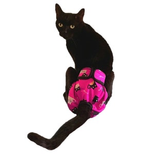 May include: A black cat wearing a pink and black cat-print diaper. The diaper has a black elastic waistband and adjustable straps.