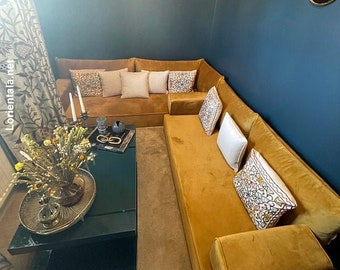 May include: A mustard yellow sectional sofa with a variety of patterned throw pillows. The sofa is in a room with a dark blue wall and a gold metal wall decor.