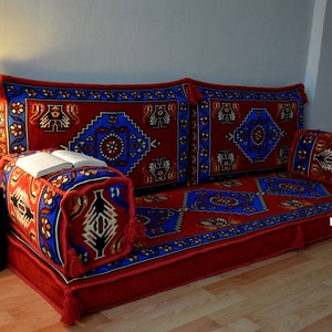 Puede incluir: Un coj&iacute;n de suelo rojo y azul con un coj&iacute;n de respaldo a juego y una almohada m&aacute;s peque&ntilde;a. Los cojines est&aacute;n dispuestos en una configuraci&oacute;n similar a un sof&aacute;.