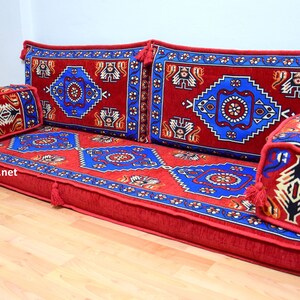 Puede incluir: Un coj&iacute;n de suelo rojo, azul y dorado con motivos y almohadas a juego. El coj&iacute;n est&aacute; hecho de una tela suave y mullida y tiene un dise&ntilde;o turco tradicional.