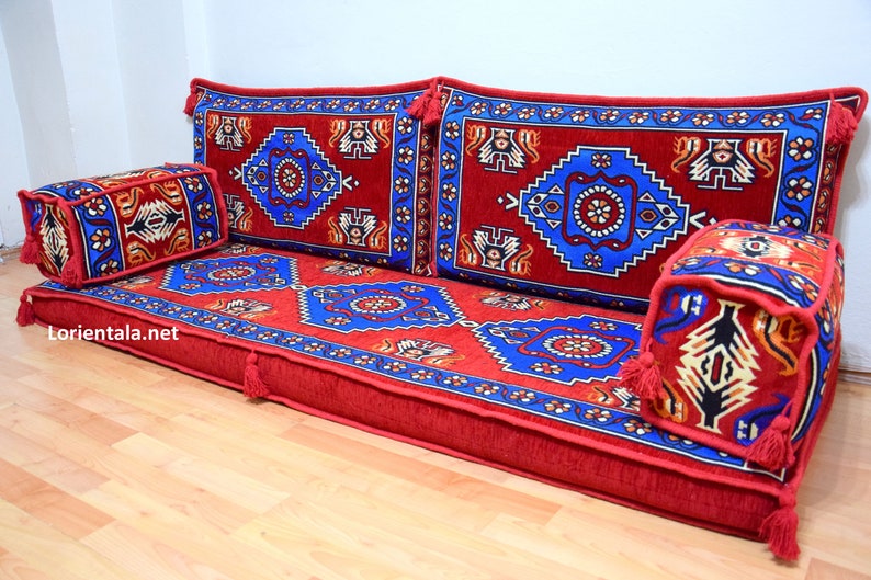 Puede incluir: Un coj&iacute;n de suelo rojo, azul y dorado con motivos y almohadas a juego. El coj&iacute;n est&aacute; hecho de una tela suave y mullida y tiene un dise&ntilde;o turco tradicional.